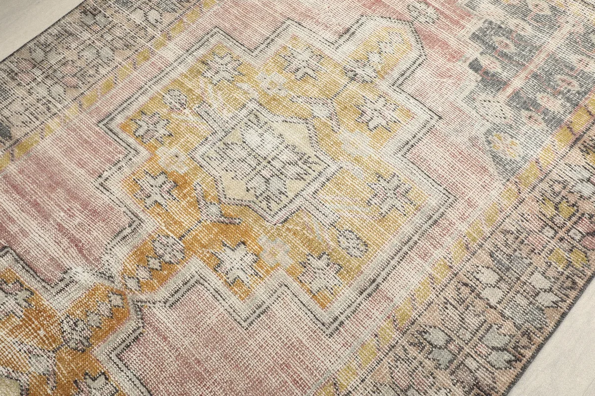 Close-up of the central medallion design, highlighting the gold, pink, and cream geometric motifs and natural wear.