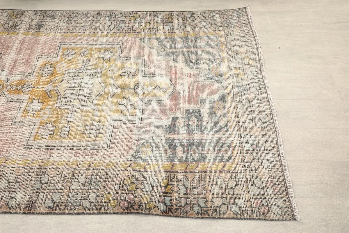 Overhead view showing one end of the rug, with its pink, gold, and charcoal geometric border patterns.