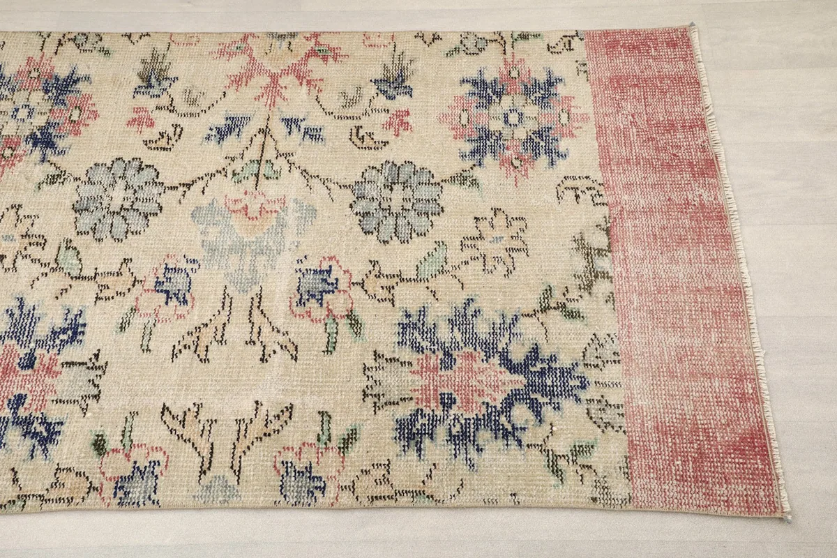 Detail view of the rug's ivory field with rose and blue floral motifs and the rose border.
