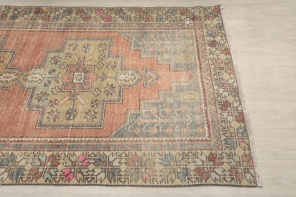 Close-up of the rug's border with geometric motifs in beige, pink, and olive tones
