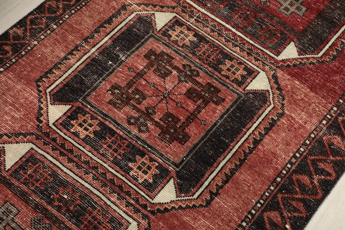 Macro detail of a central black geometric motif within a medallion on the red vintage rug.