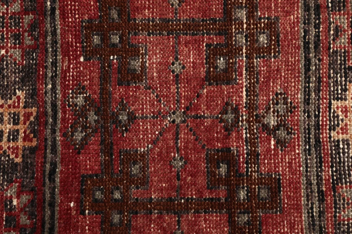 Close-up showing the hand-knotted wool pile and detailed red, black, and tan threads.