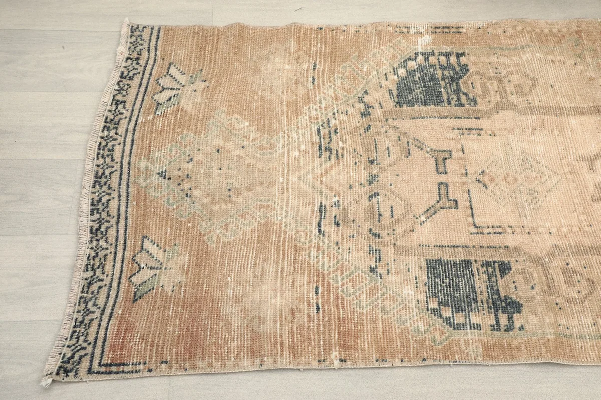 Close-up detail of one end of the rug, showing faded blue and tan tribal motifs and the edge.