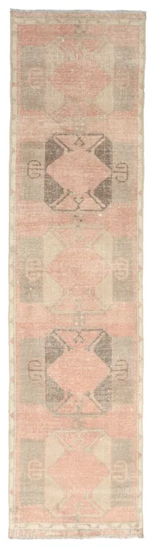 Full overhead view of a faded rose, gray, and beige geometric Anatolian runner on a white background.
