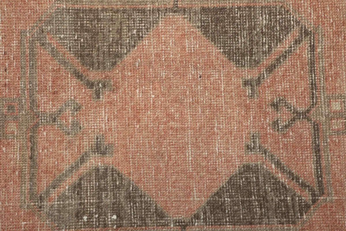 Extreme close-up of a central geometric motif in faded rose and charcoal, highlighting knot detail.