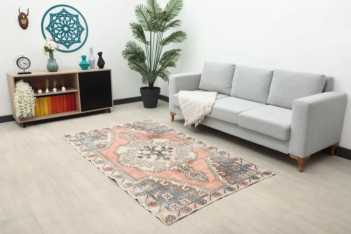 Small rose and blue vintage rug placed in a modern living room with a gray sofa and plant