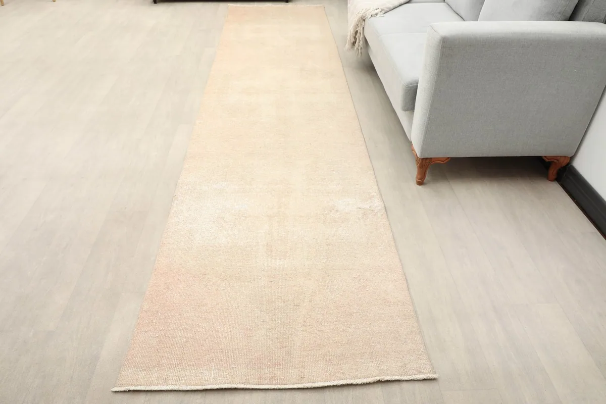 Beige and rose vintage runner rug extending along a light-colored floor next to a gray sofa.