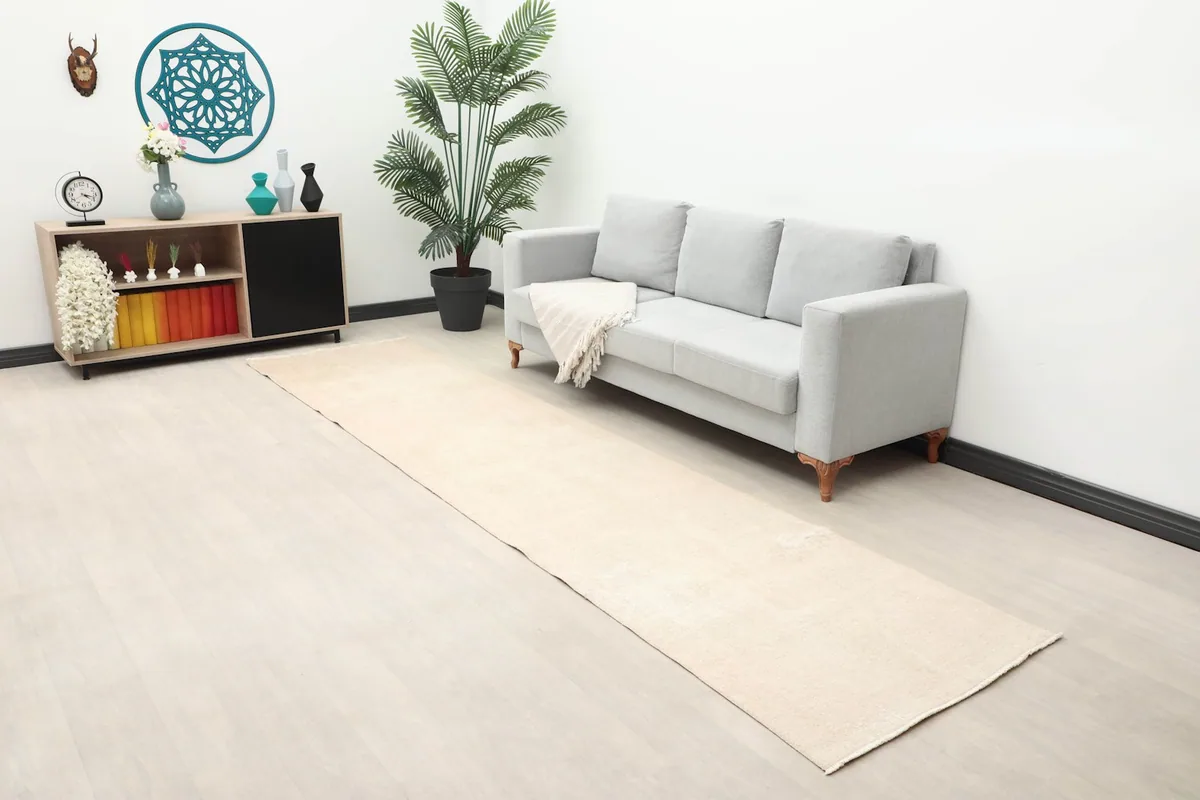 Wide view of the beige and rose runner rug in a living space with a gray sofa and decorative elements.