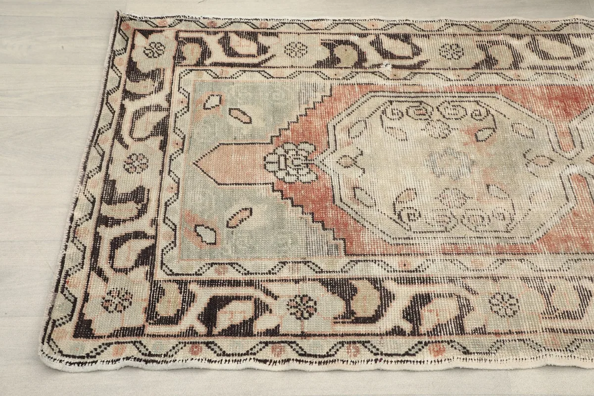Detailed shot of the rug's geometric patterns and color variations, including the beige field and rust accents.