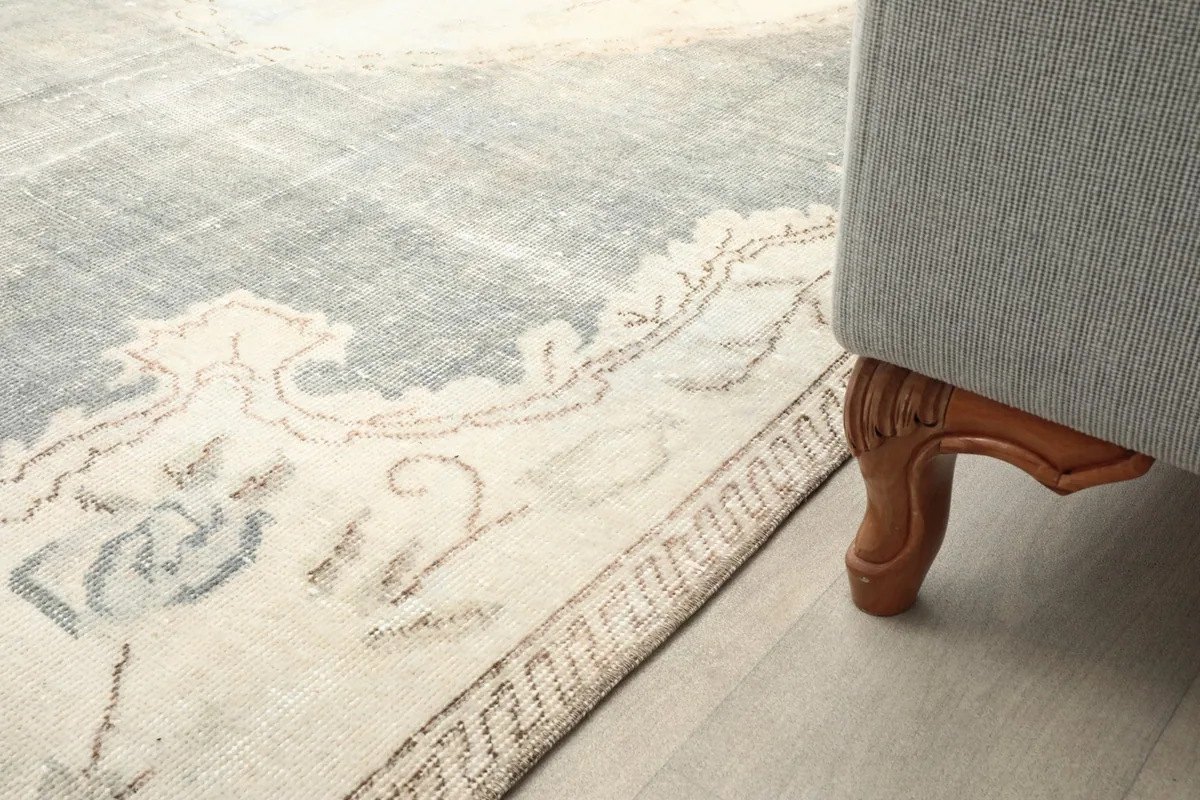 Close-up of the rug's border and corner next to a wooden sofa leg, showing color and wear