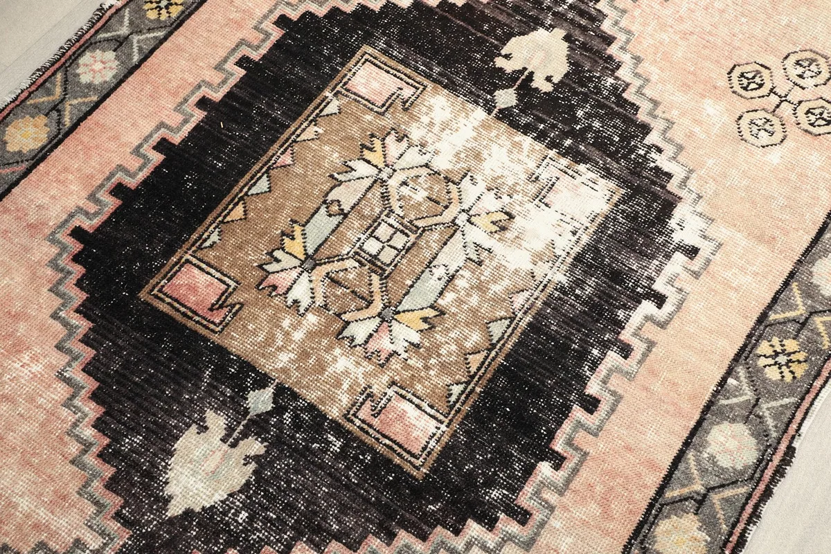 Close-up of a black geometric medallion with inner patterns in beige, pink, and yellow