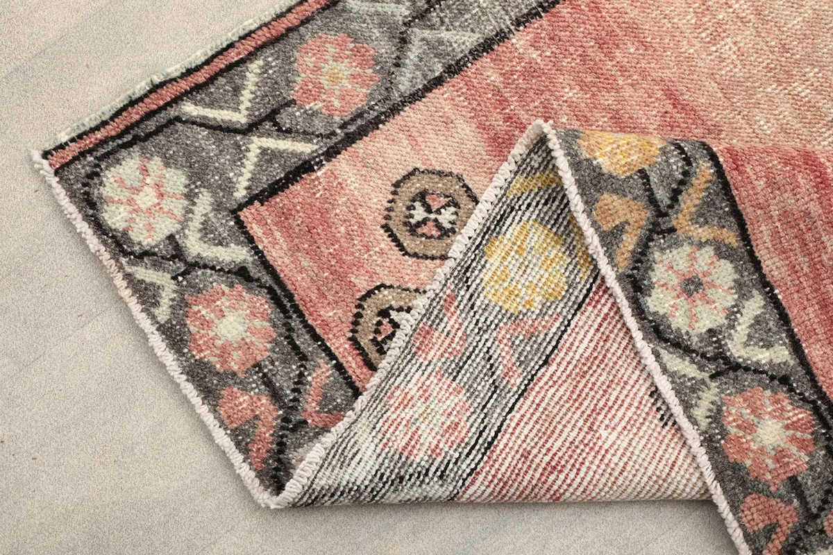 Folded corner of the runner rug, showing the rose field, gray border, and fringe