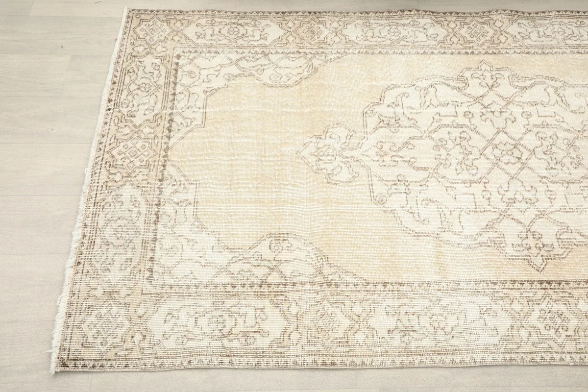 Angled view focusing on the central medallion and border patterns of the ivory and beige rug.