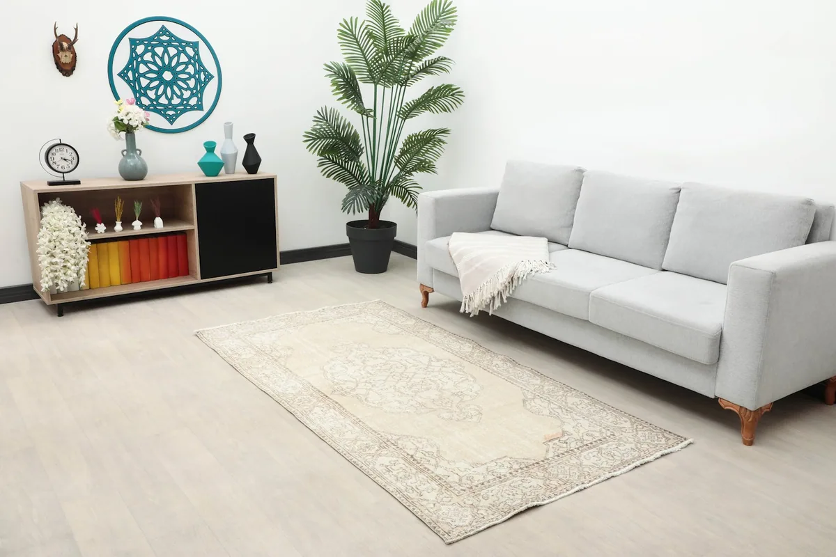 Ivory vintage rug placed in a living room setting with a gray sofa and wooden cabinet.