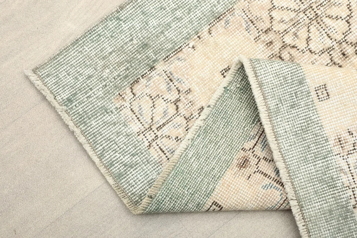 Folded section of the rug, revealing the texture of the gray-green border and ivory field