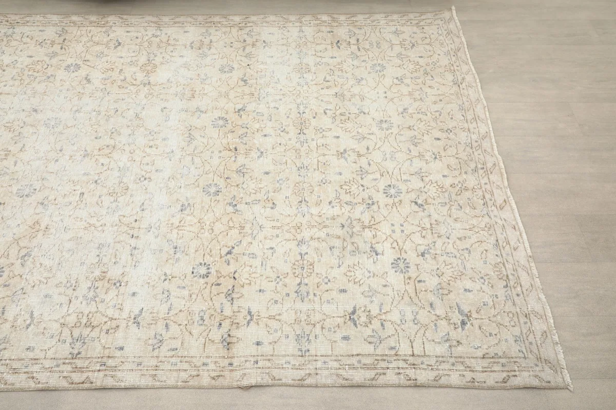 Close-up angled view of the cream rug, showing the faded floral and geometric patterns.