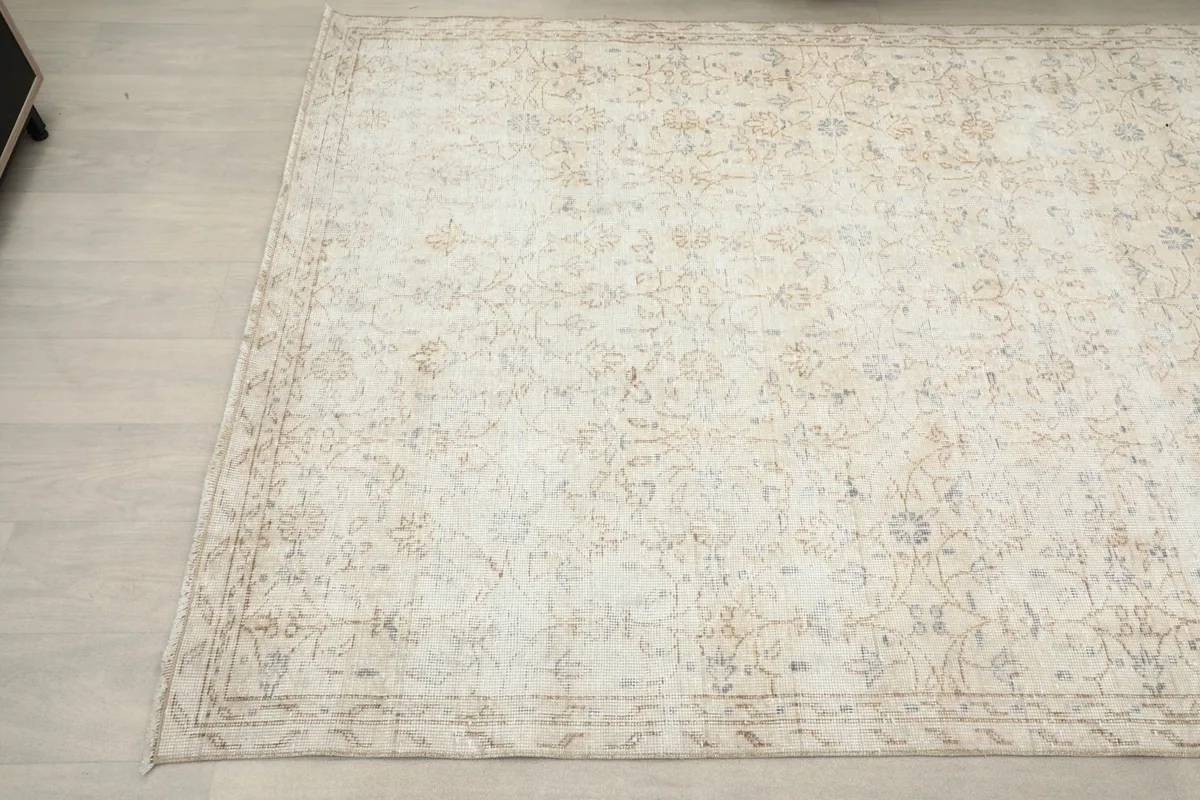 Angled view of the cream rug, highlighting the subtle tan and blue motifs and border.