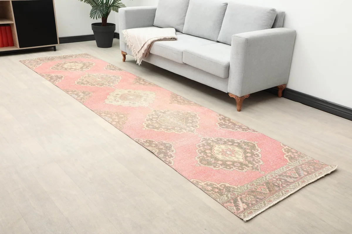 Angled view of the rose and brown vintage runner rug extending across a room with light flooring.
