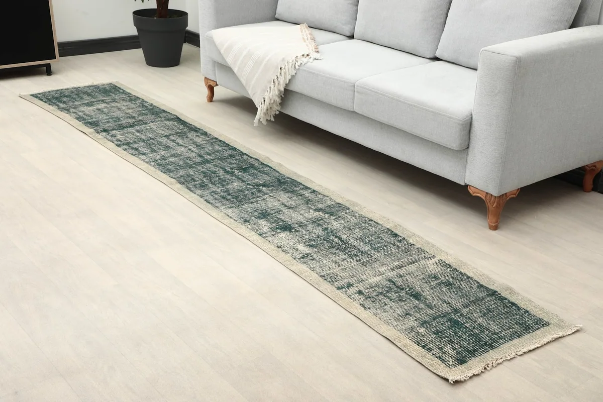 Angle view of the green and beige runner rug on a light floor, showing its length next to a sofa.
