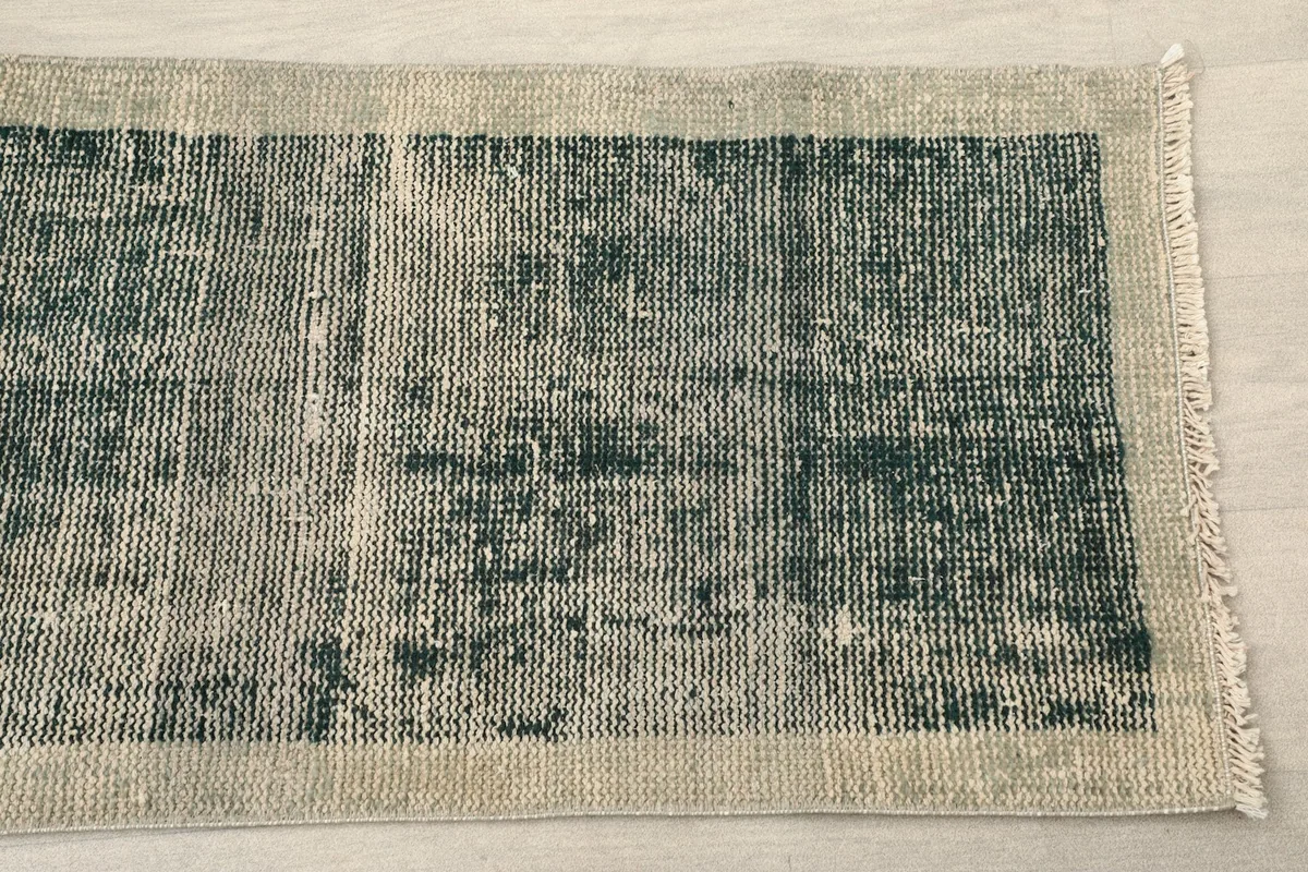 Close-up of one end of the green runner rug, highlighting the distressed texture and beige border.