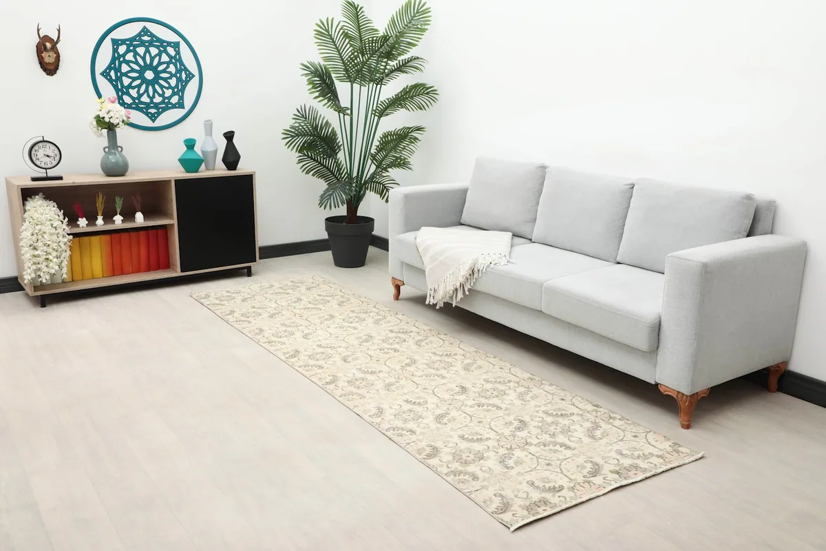Long view of the cream runner rug in a room with a sofa, plant, and decorative shelf