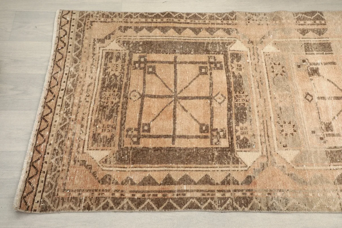 Detailed view of the complex tribal and geometric motifs in brown and charcoal at one end of the rug