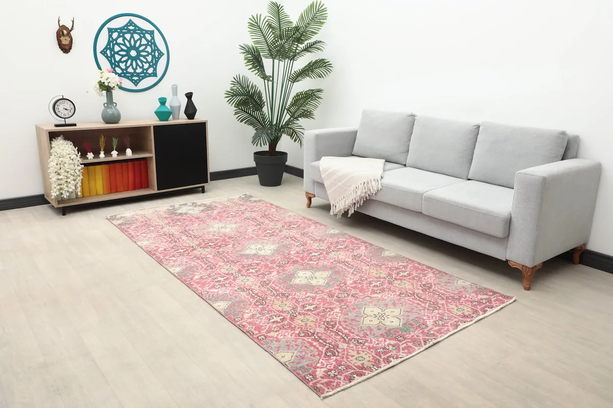 Vintage rose and gray rug placed in a modern living room with a gray sofa and wooden console