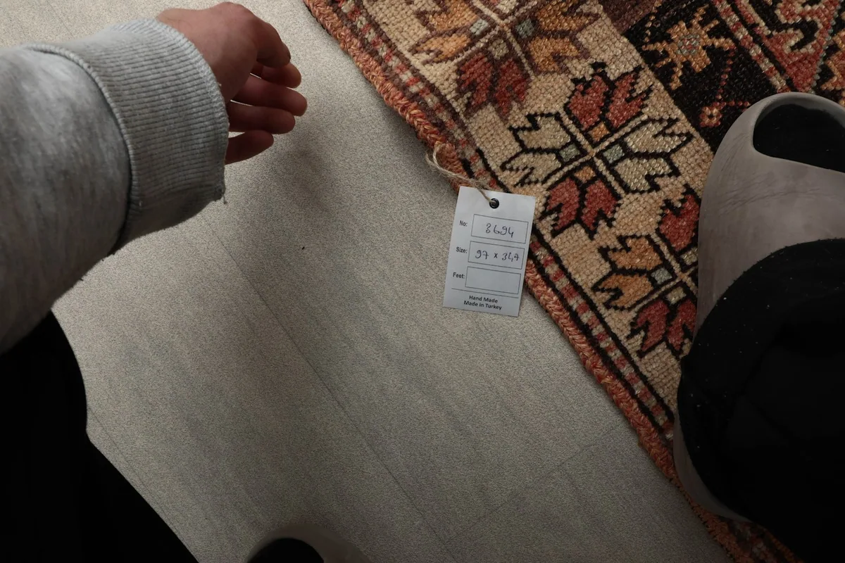 Hand next to the rug's label, showing the dimensions 3'2" x 11'5" (97 x 347 cm)