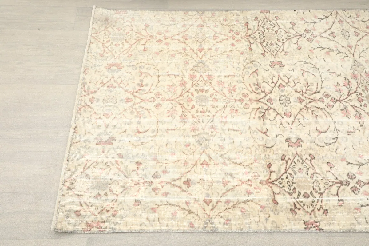 Another angle view of the ivory and rose vintage Anatolian rug, showing the faded design and texture.