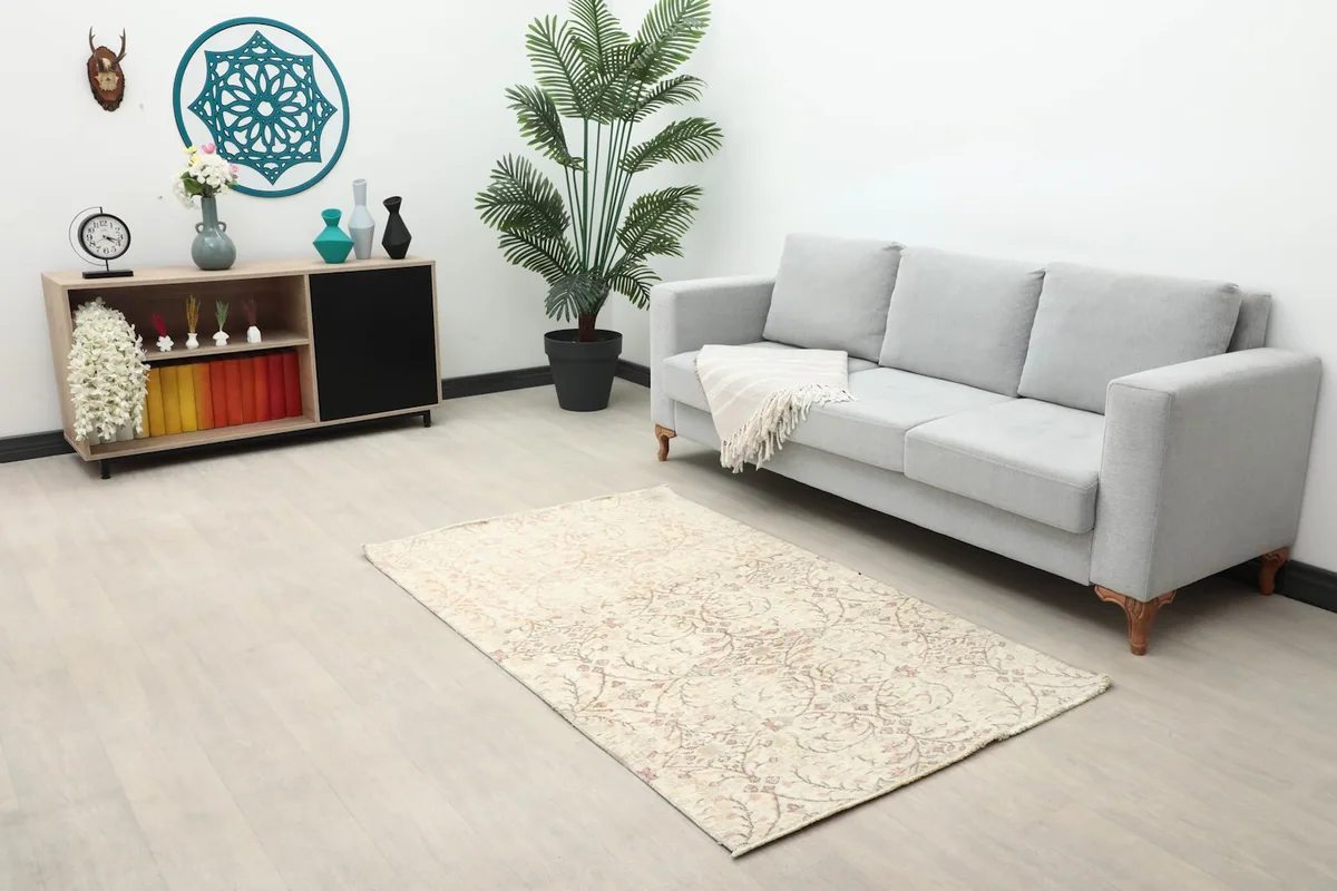Ivory and rose vintage Anatolian rug placed in a living room setting with a gray sofa and wooden cabinet.