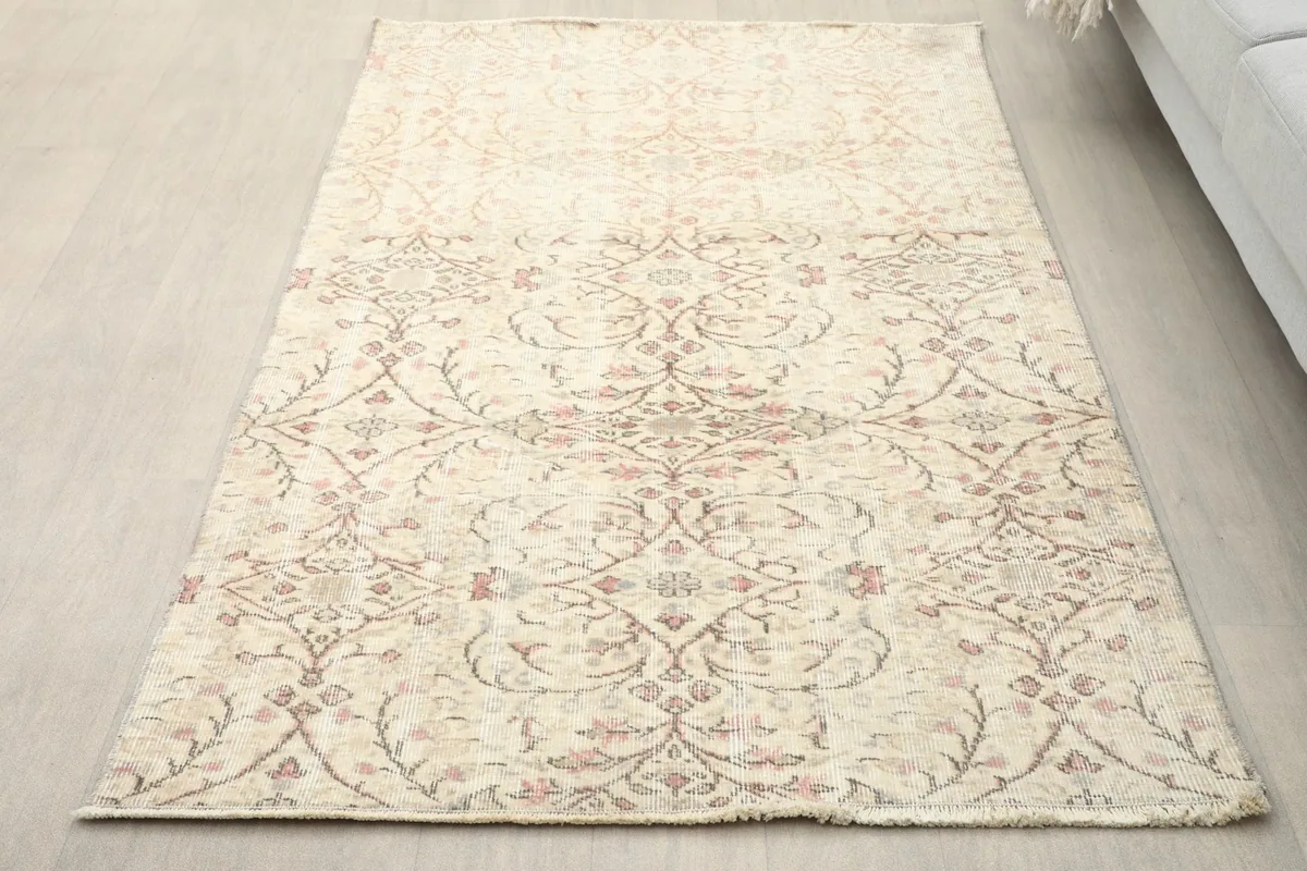 Overhead view of the ivory and rose vintage Anatolian rug on a light wooden floor, showcasing its full pattern.