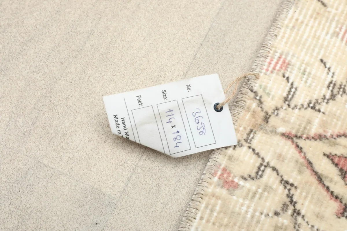 Product tag displaying the rug's dimensions (114 x 184 cm) and origin on the rug's surface.