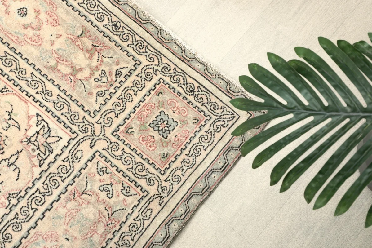 View of the rug's border with a green plant, showing the geometric and floral patterns in gray and rose