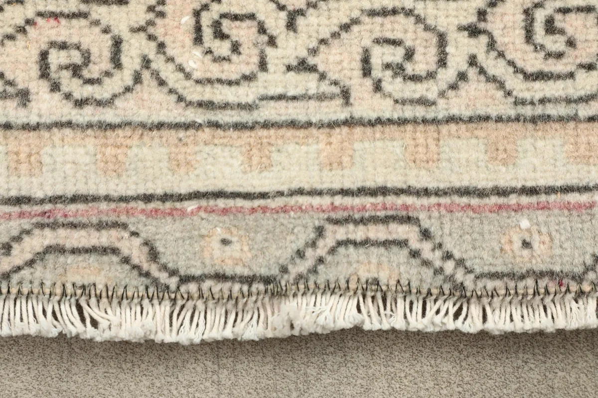 Close-up of the rug's fringe and a section of the border pattern showing rose and gray details