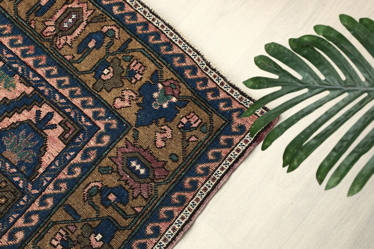 Angled shot of the rug's border with a green plant leaf in the foreground, showing texture
