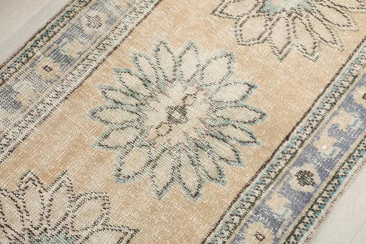 Overhead detail of a central floral motif with subtle blue and green tones on the beige background.