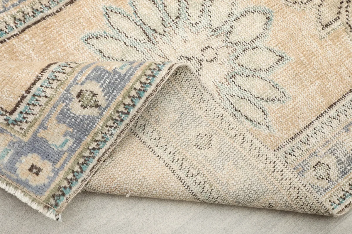 Folded corner showing the rug's reverse side and the cotton foundation, with a glimpse of the fringe.