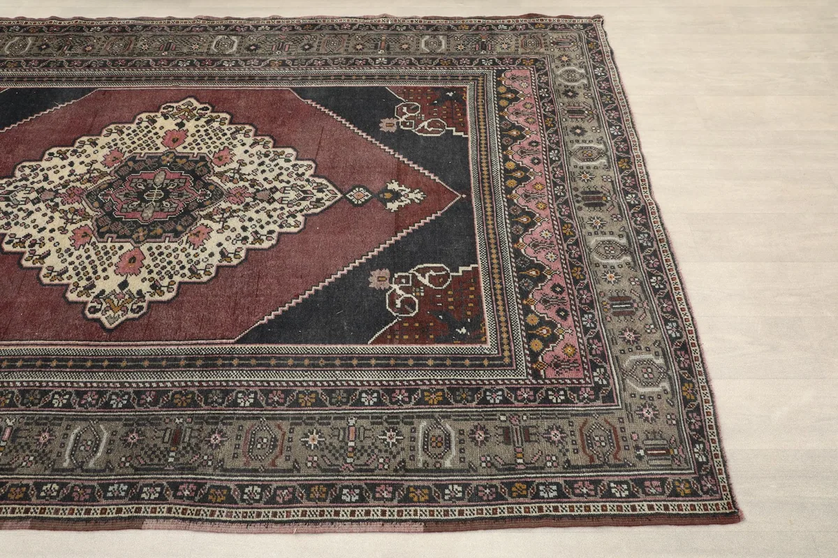 Detailed view of the rug's border and corner, showing geometric and floral motifs in gray and pink
