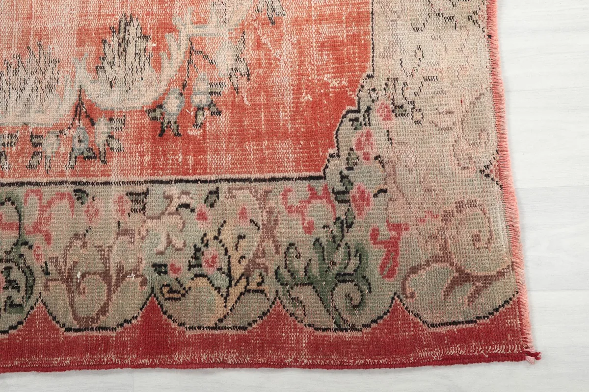 Detail of the rust rug's ornate border with beige and green floral patterns.