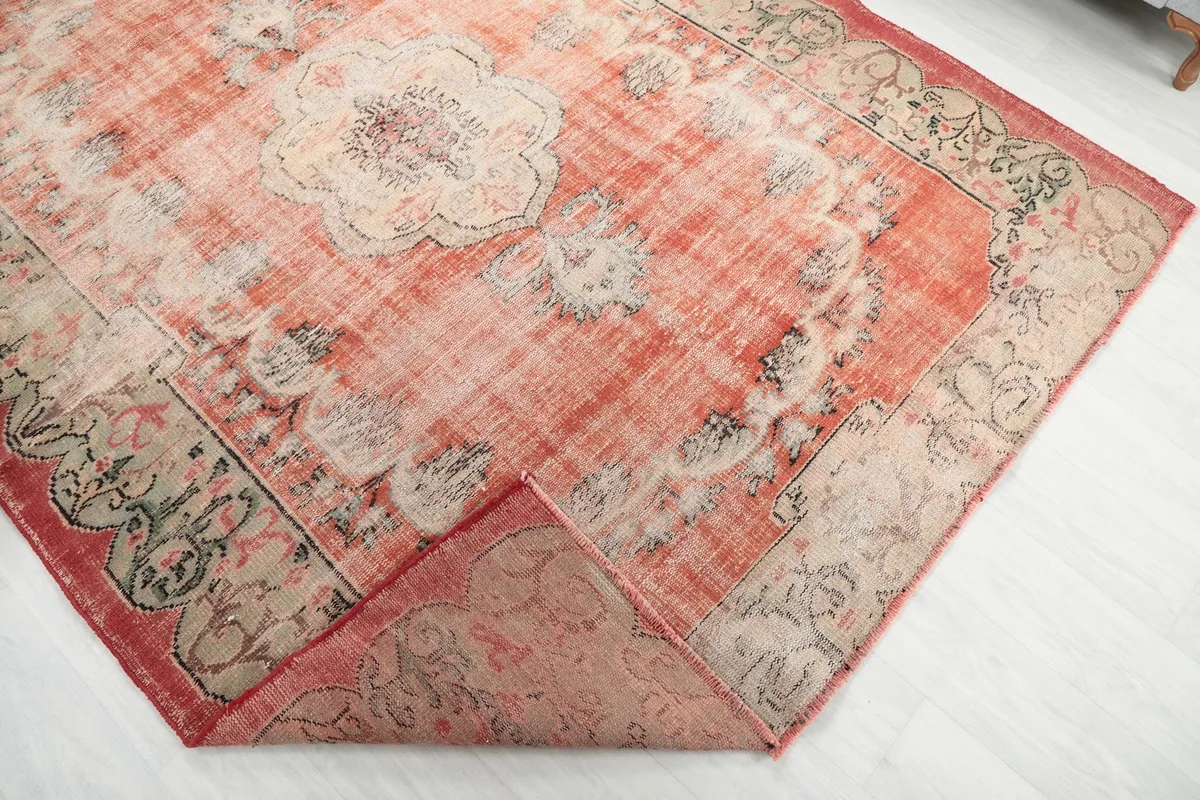 Corner of the rust rug folded back, revealing the underside of the hand-knotted wool pile.