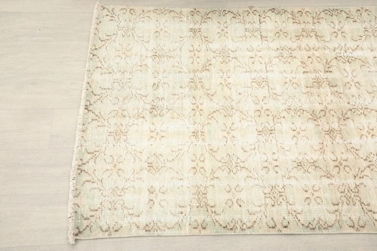 Angled view of one end of the beige rug, showing the subtle color variations and fringe.