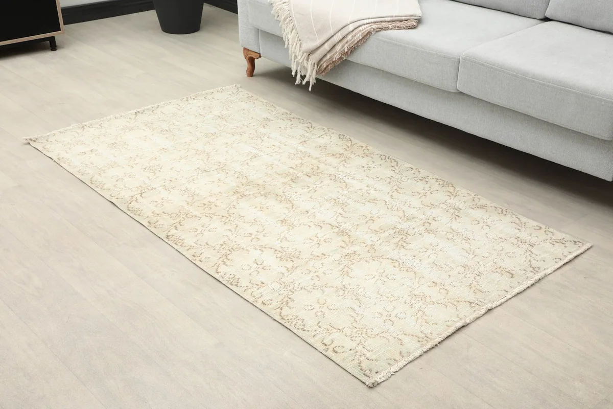 Angled view of the beige floral rug in a living room, showing its placement next to a sofa.