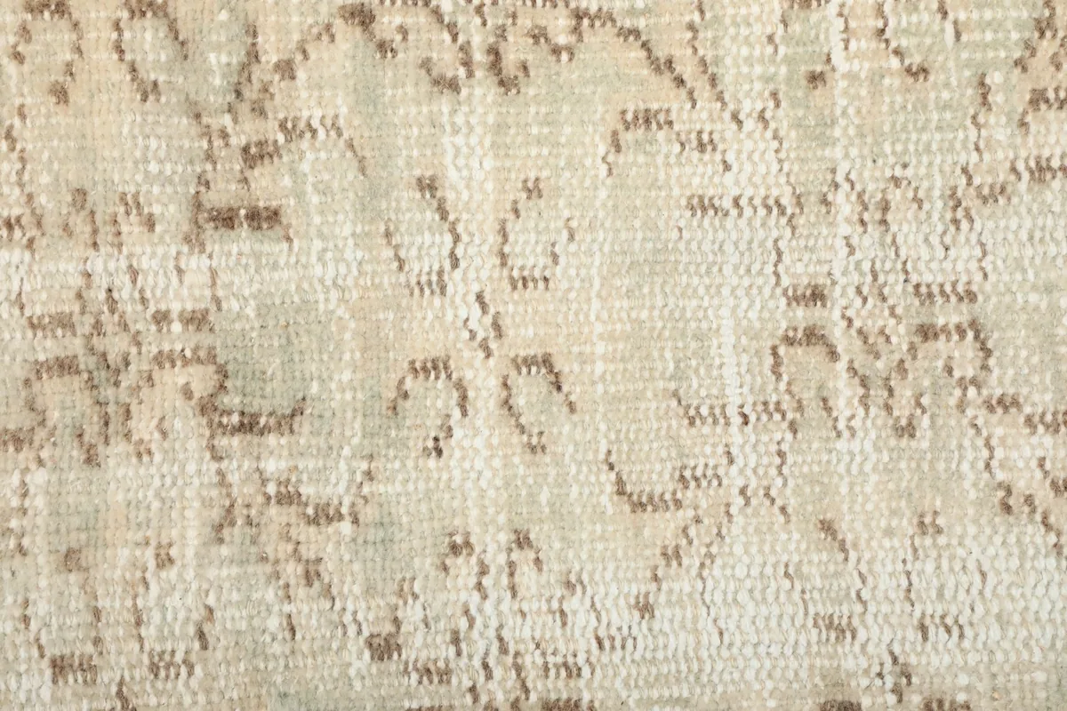 Extreme close-up of the hand-knotted wool pile and the detailed tan patterns on the beige field.