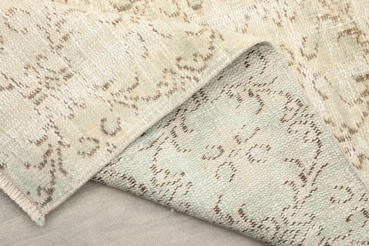 View of the rug's back and folded edge, showing the tightly woven cotton foundation.