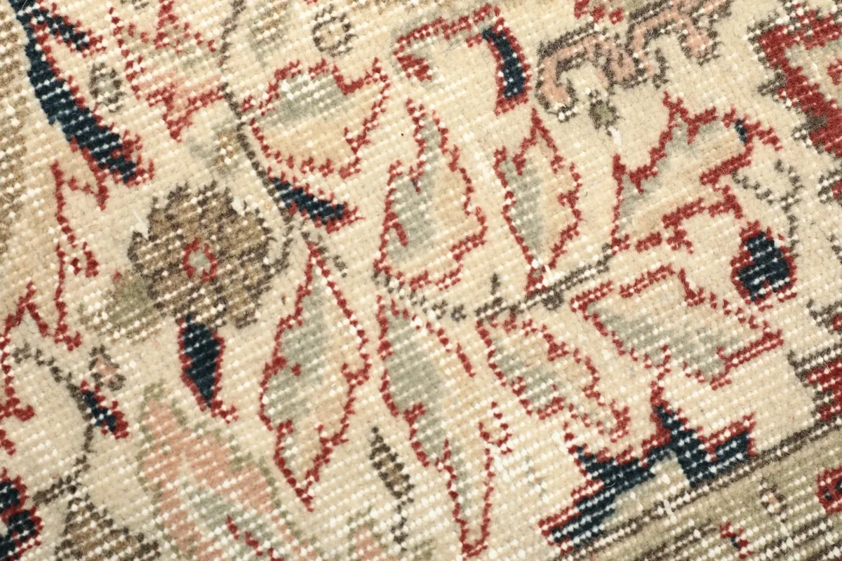 Detailed view of the low wool pile and intricate knotting in beige and red tones
