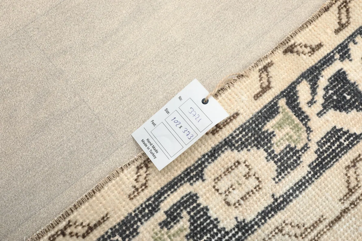Close-up of the rug's back side, showing the cotton foundation and a tag with dimensions.