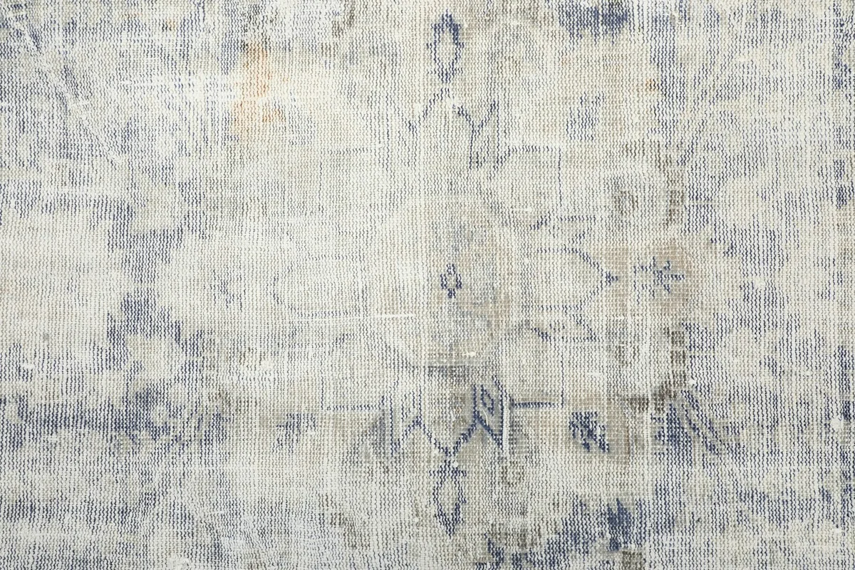Detailed close-up of the central geometric motif and the distressed ivory and blue wool pile.