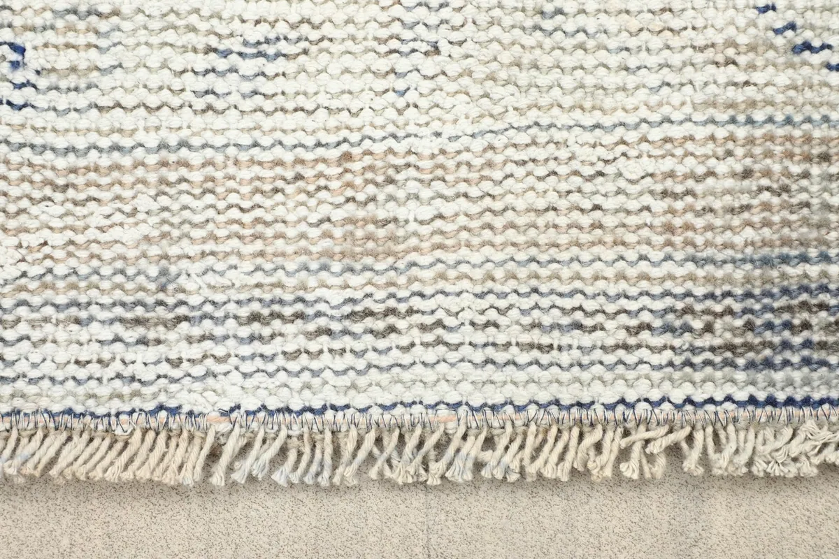 Close-up view of the short, natural fringe and the woven edge of the vintage rug.