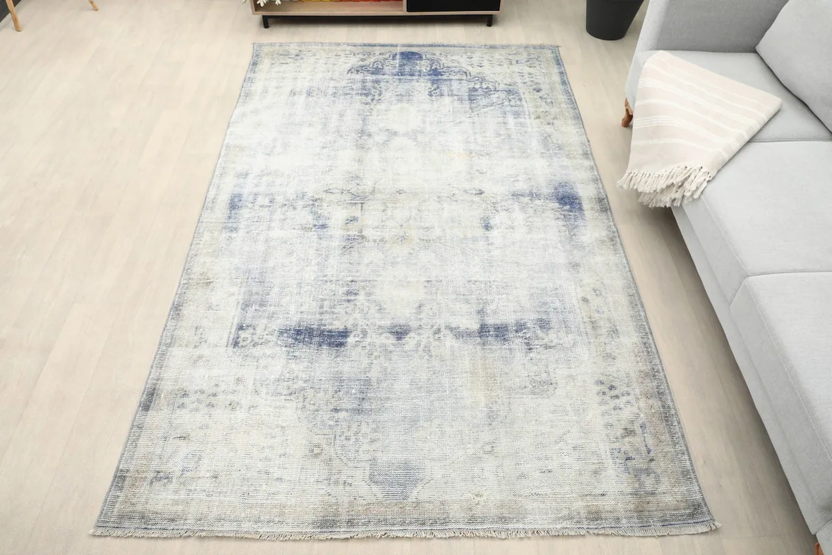 Overhead view of the ivory and blue vintage rug placed in a modern room setting on a light wood floor.