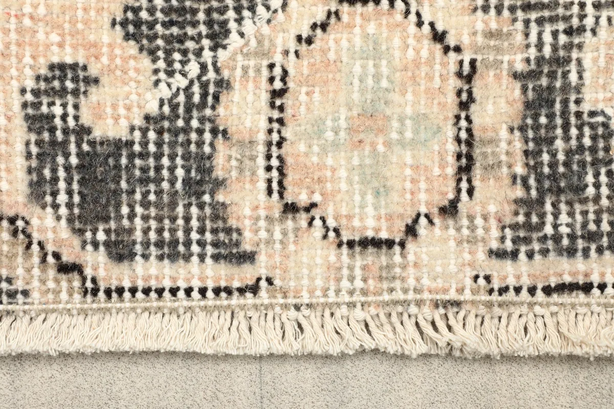 Close-up detail of the fringe and low pile texture of the vintage wool rug